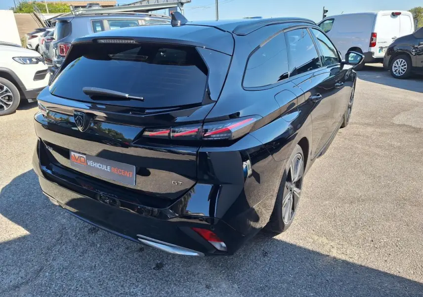 Vue 3/4 arrière droite d'une Peugeot 308 SW Hybrid 145 GT noire avec barres de toit et jantes alliage 18 pouces.