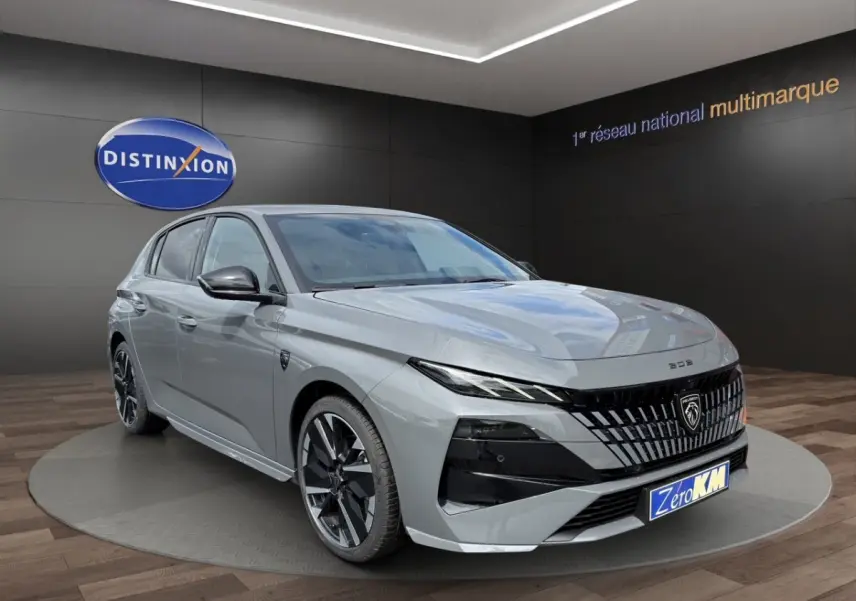 Peugeot 308 gris clair vue 3/4 avant droit, calandre noire distinctive et jantes noires brillantes.