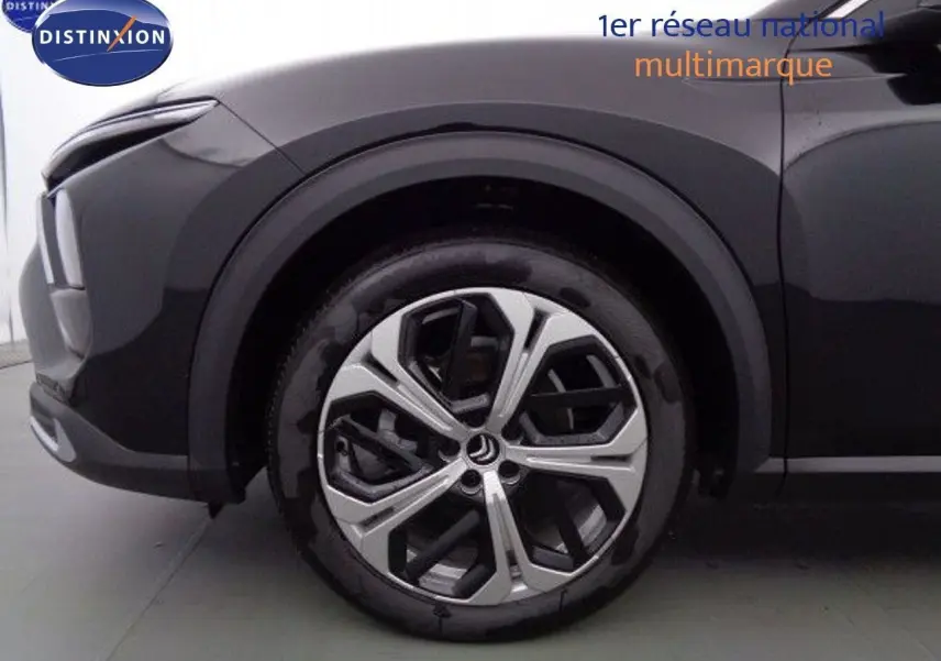 Gros plan sur la roue avant gauche du Citroën C5 X noir métal, mettant en valeur sa jante moderne à motifs géométriques.