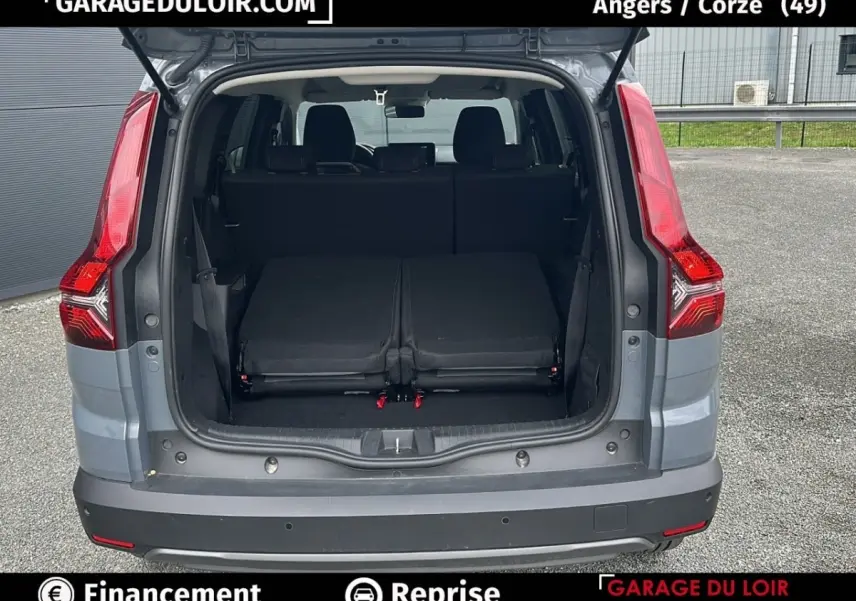 Vue arrière du coffre ouvert d’un Dacia Jogger gris, montrant les sièges arrière rabattus et les feux arrière rouges.