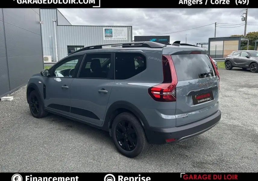 Vue 3/4 arrière droite d'un Dacia Jogger Extreme+ Hybrid 140 gris avec jantes noires, en extérieur sur parking.