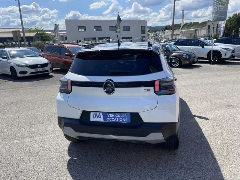 Vue arrière d'une Citroën C3 Nouvelle blanche 2025 avec logo central noir et feux arrière distinctifs, stationnée en extérieur.
