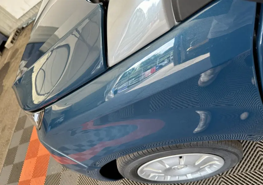 Gros plan sur l'aile avant gauche bleu d'une Aixam Ambition 0.5 City Pack avec rétroviseur caméra côté conducteur.