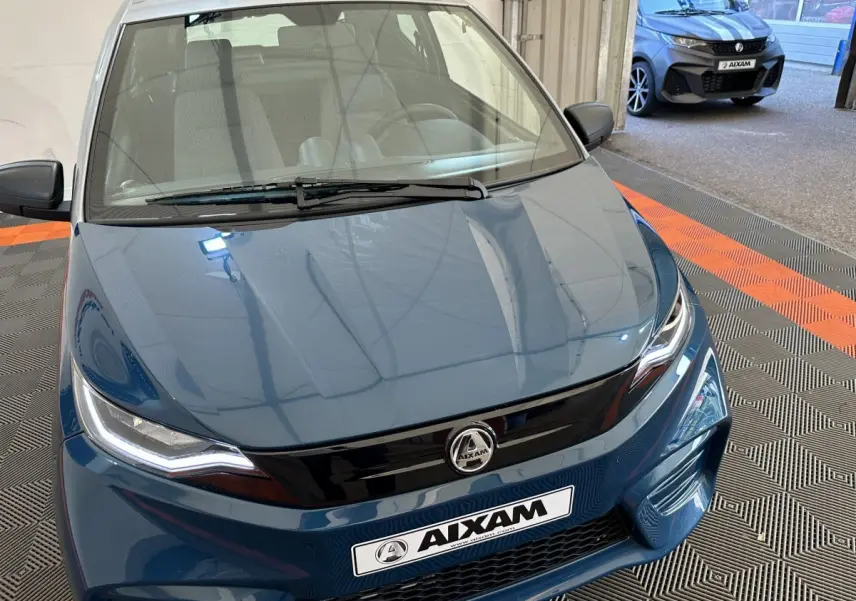 Vue avant rapprochée d'une Aixam Ambition 0.5 City Pack bleu 2025 avec calandre noire et phares LED marqués.