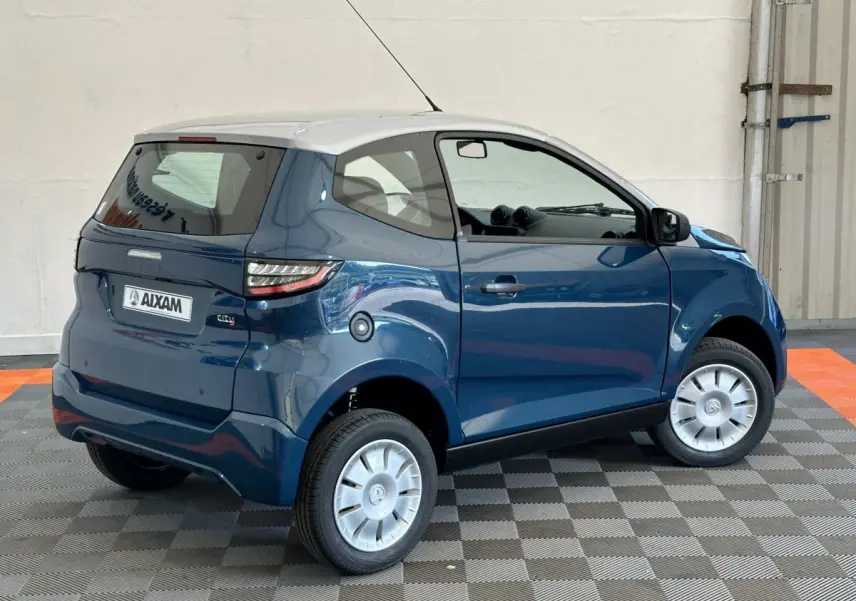 Vue 3/4 arrière droite d'une Aixam Ambition 0.5 City Pack bleu avec toit blanc et rétroviseur caméra côté gauche.