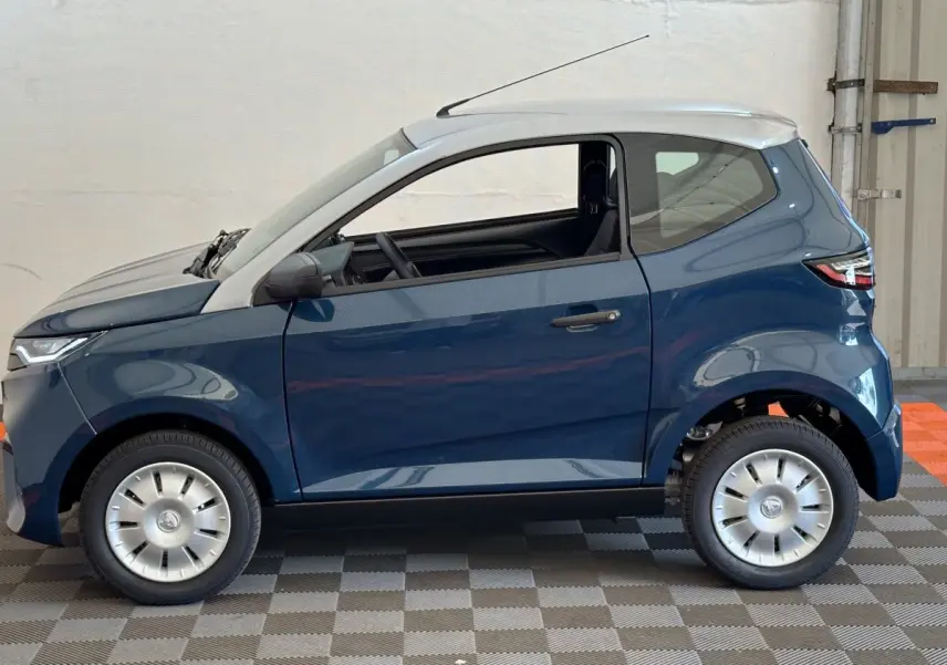 Profil côté gauche de l'AIXAM AMBITION 0.5 CITY PACK 2025 bleu avec toit blanc et rétroviseur caméra conducteur.