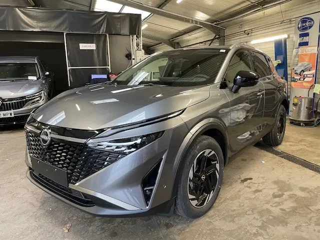 Vue 3/4 avant droit du Nissan Qashqai 2025 gris squale métal avec calandre noire et phares LED fins.
