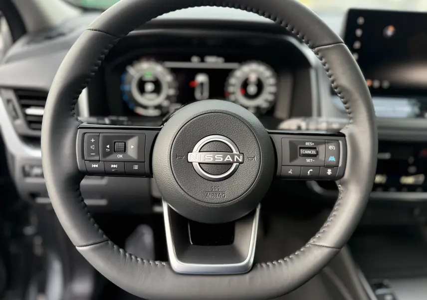 Vue rapprochée du volant cuir noir du Nissan Qashqai 2025 avec commandes intégrées et tableau de bord numérique flou en arrière-plan.