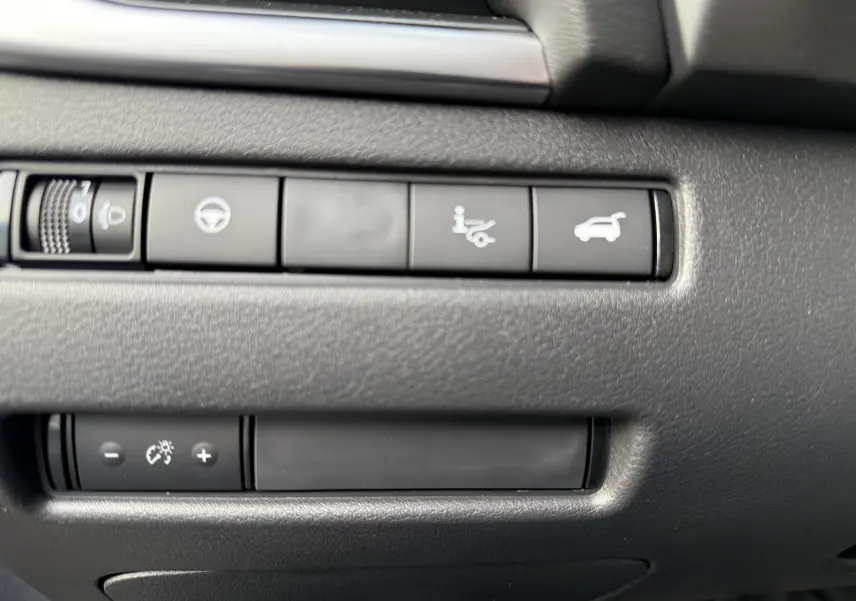 Gros plan sur les boutons de commande intérieurs noirs du Nissan Qashqai 1.5 E-POWER gris, avec icônes blanches lumineuses.