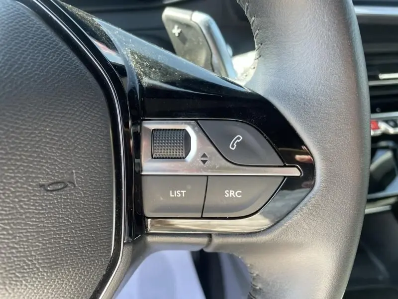 Gros plan sur les commandes gauche du volant en cuir noir du Peugeot 2008 gris métal 2025, avec boutons de téléphone et volume.