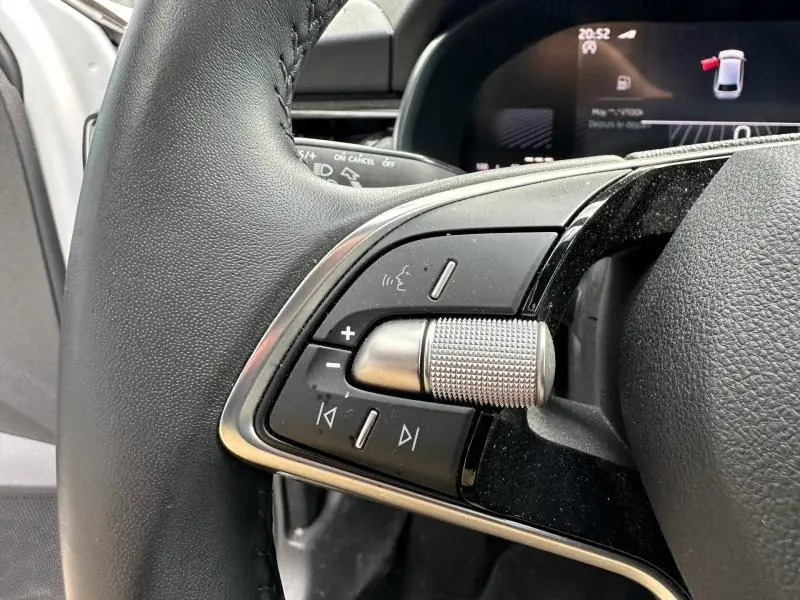 Gros plan sur les commandes audio au volant cuir noir d'une Skoda Scala blanc cristal, avec écran numérique en arrière-plan.