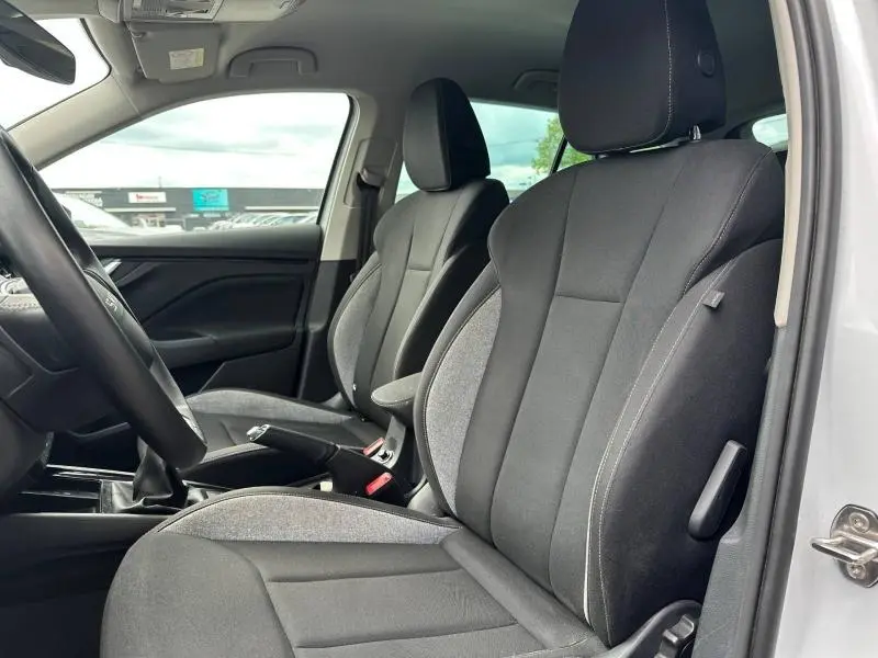 Vue intérieure côté gauche des sièges avant tissu noir et gris d'une Skoda Scala blanc cristal avec volant cuir et levier de vitesses manuel.