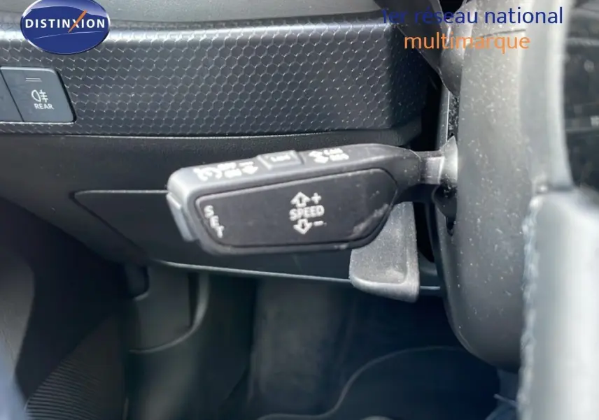 Gros plan sur la commande de régulateur de vitesse à gauche du volant d’une Audi A1 Sportback noire, intérieur sombre.