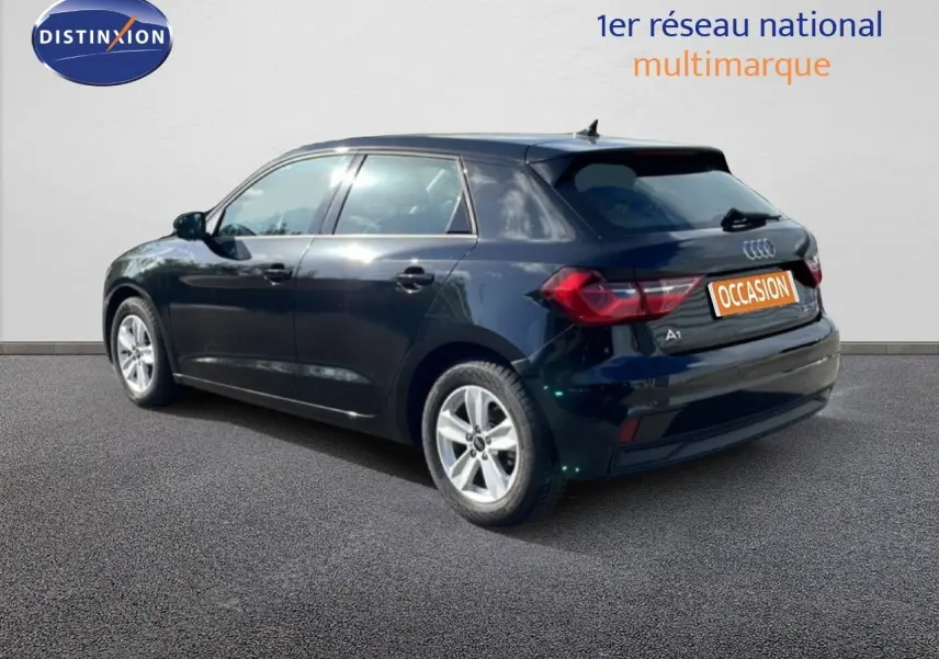 Audi A1 Sportback noir mythe métal vue 3/4 arrière droit sur sol gris avec logo Distinxion en arrière-plan.