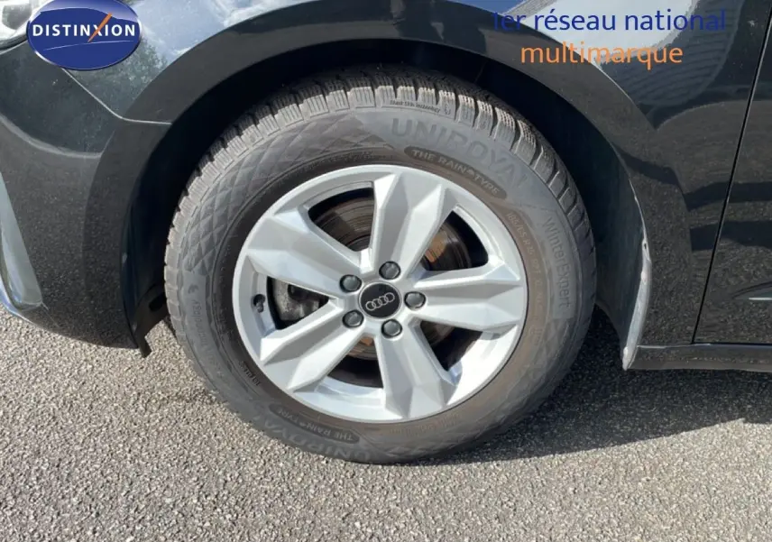 Gros plan sur la roue avant gauche d’une Audi A1 Sportback noire Mythe Metal avec jante argentée cinq branches.