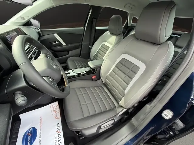 Vue intérieure côté conducteur de la Citroën C4 hybride 2025 bleu, sièges tissu gris avec volant cuir multifonctions.