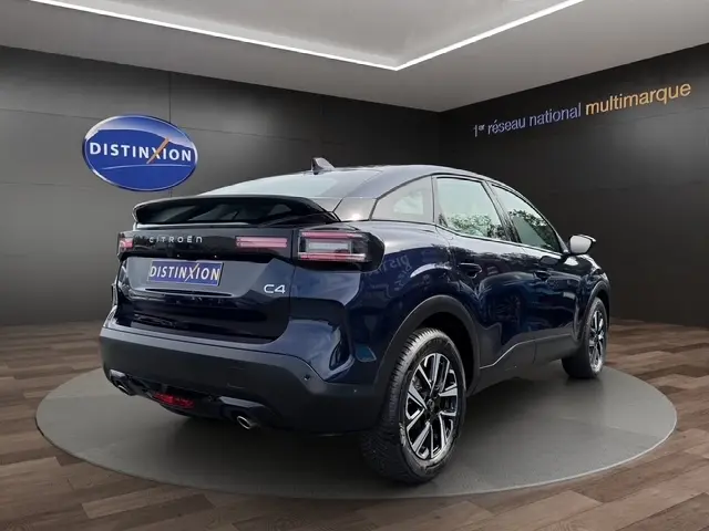 Vue 3/4 arrière droite d'une Citroën C4 hybride bleu foncé avec jantes alliage et feux LED dans un showroom.