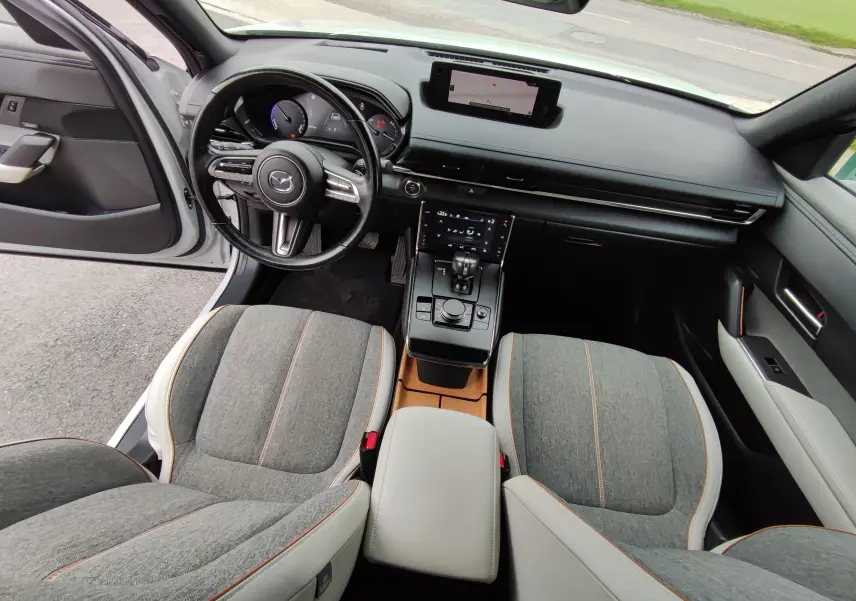 Vue intérieure avant du Mazda MX-30 gris clair 2023, avec sièges tissu gris, tableau de bord noir et écran tactile central.