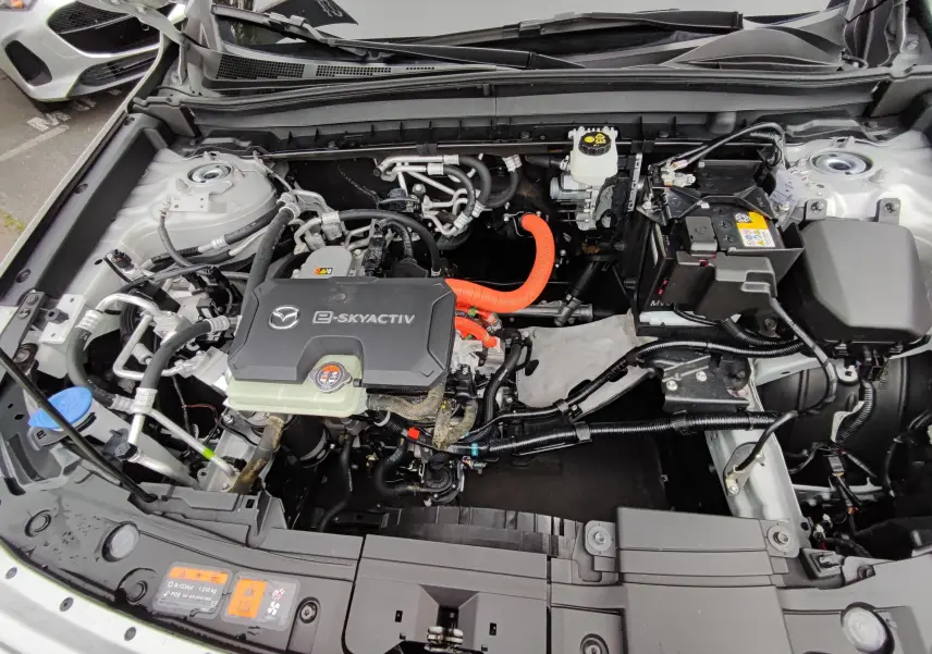 Vue plongeante sur le compartiment moteur électrique gris clair du Mazda MX-30 2023 avec câbles orange visibles.