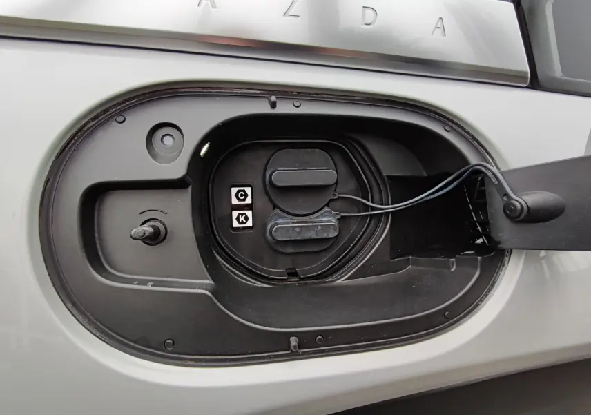 Gros plan sur la trappe de recharge électrique ouverte du Mazda MX-30 gris clair, montrant les connecteurs de charge.