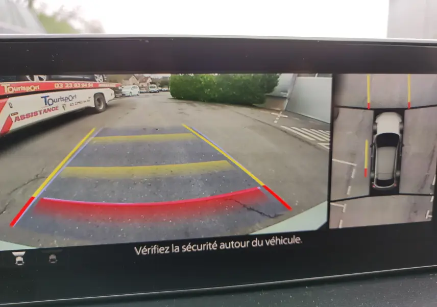 Vue de la caméra de recul et vue aérienne du Mazda MX-30 gris clair en stationnement, avec repères de guidage colorés.
