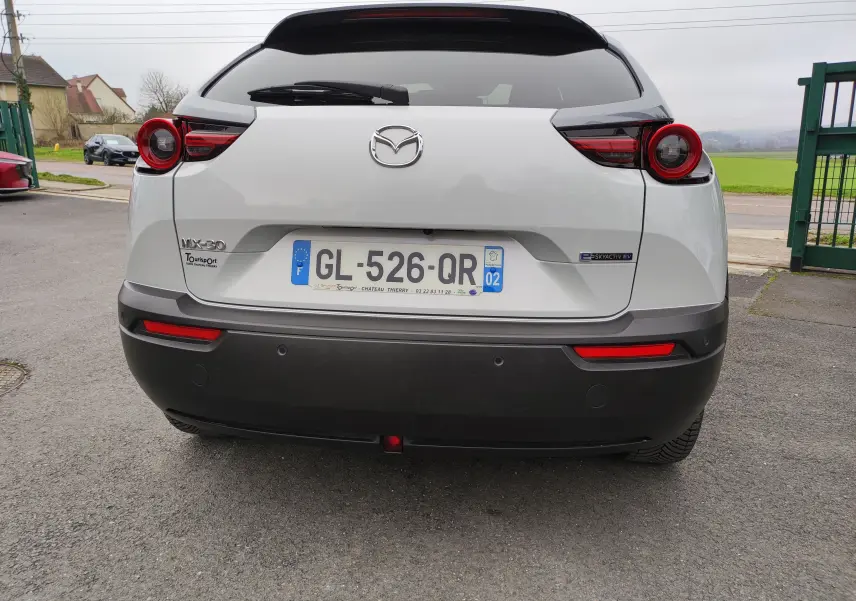Vue arrière d'une Mazda MX-30 gris clair 2023, avec feux arrière ronds et badge électrique E-SKYACTIV EV visible.