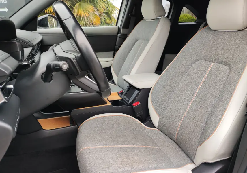 Vue intérieure côté conducteur du Mazda MX-30 gris clair 2023, sièges tissu gris avec surpiqûres orange et accoudoir central.