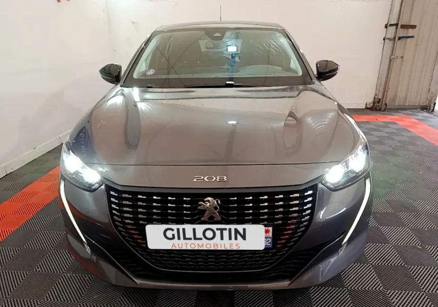 Vue frontale d'une Peugeot 208 gris foncé avec phares LED allumés dans un garage.