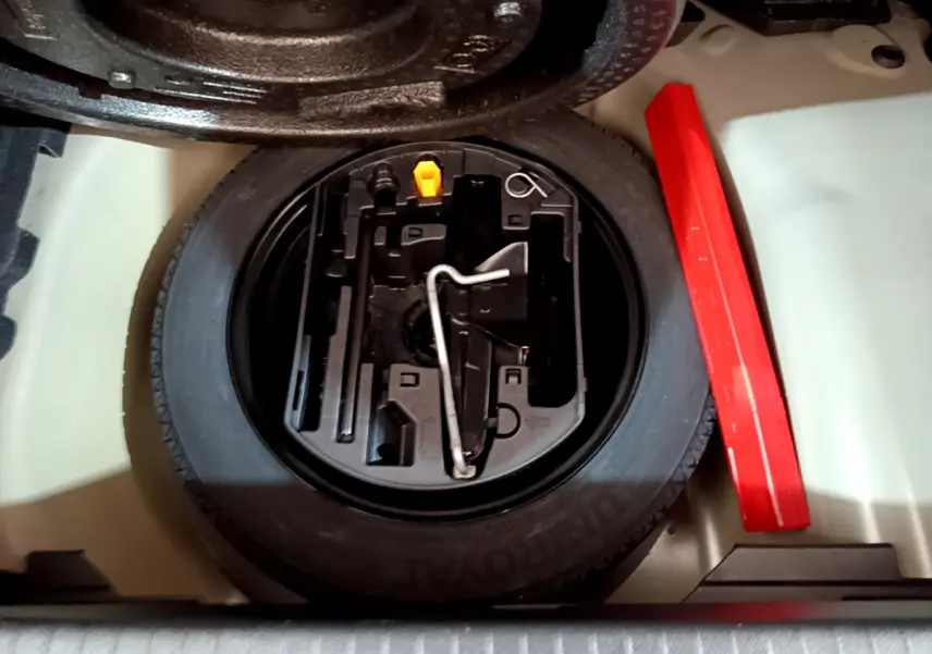 Vue rapprochée de la roue de secours et des outils de bord dans le coffre d'une Peugeot 208 gris foncé 2022.