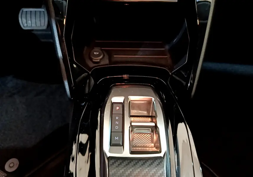 Vue plongeante sur la console centrale noire brillante de la Peugeot 208 PureTech 100 avec sélecteur de boîte auto et bouton P.