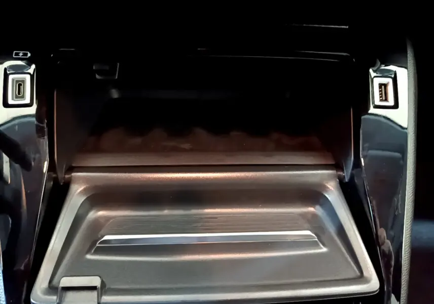 Vue rapprochée de la boîte à gants ouverte avec ports USB et finition noire brillante dans une Peugeot 208 gris foncé.