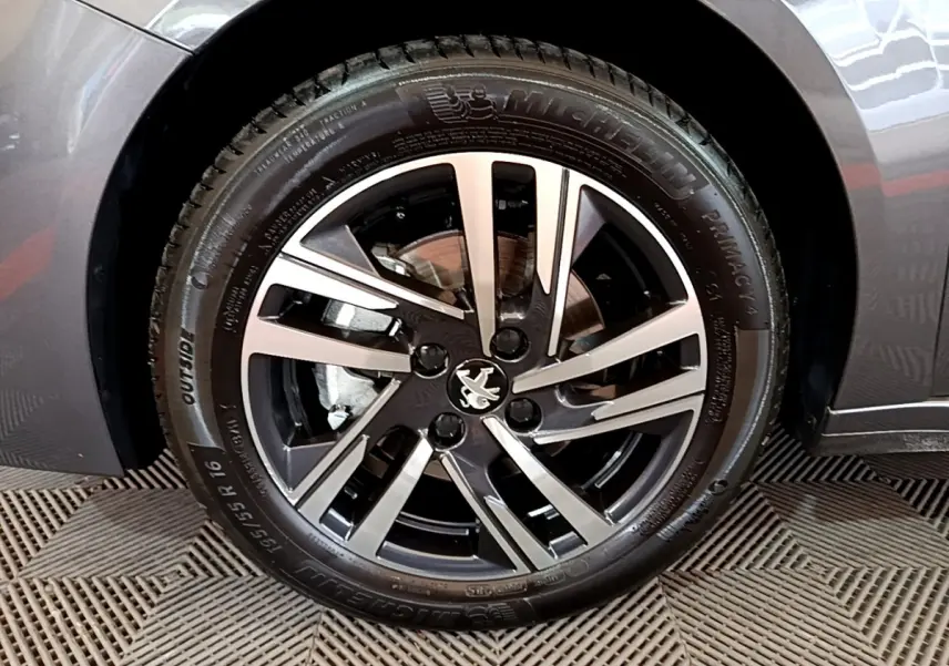 Gros plan sur la roue avant droite d’une Peugeot 208 gris foncé, avec jante alliage noire et argentée.