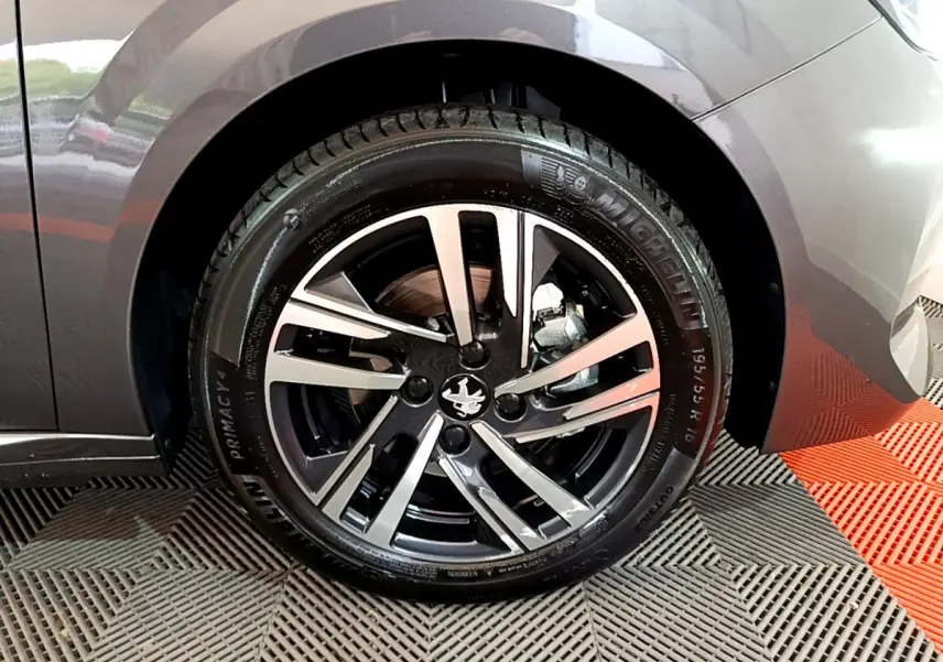 Gros plan sur la roue avant droite d’une Peugeot 208 gris foncé, jante alliage au design moderne à 5 branches doubles.