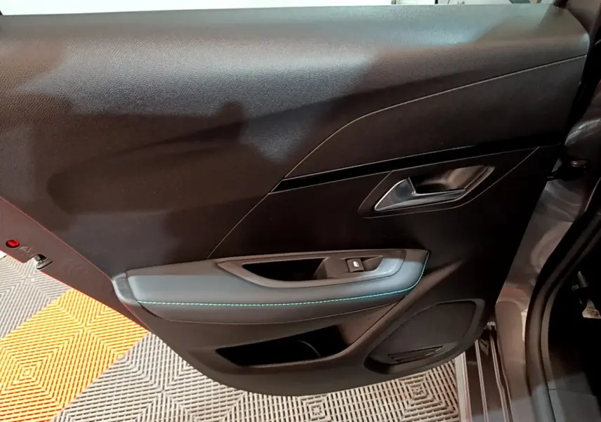 Gros plan sur la porte intérieure côté gauche de la Peugeot 208 gris foncé, avec surpiqûres bleues et poignée argentée.
