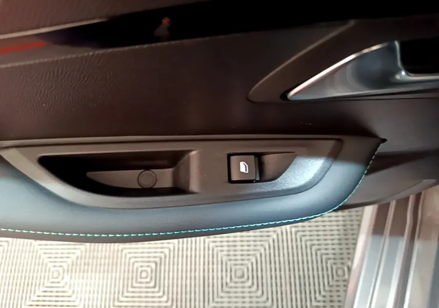 Gros plan sur la commande de verrouillage de porte côté conducteur d'une Peugeot 208 gris foncé avec surpiqûres bleues.