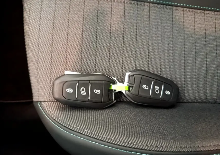 Gros plan sur deux clés noires posées sur un siège gris foncé avec surpiqûres bleues, intérieur Peugeot 208.