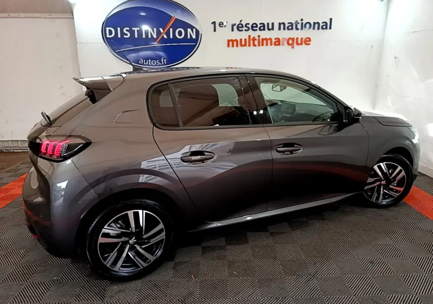 Peugeot 208 gris foncé vue de profil droit en intérieur, feux arrière LED et jantes alliage visibles.