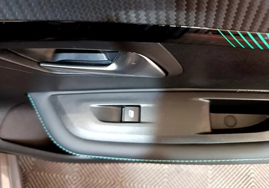 Gros plan sur la poignée intérieure et commande de vitre côté conducteur de la Peugeot 208 gris foncé avec surpiqûres bleues.