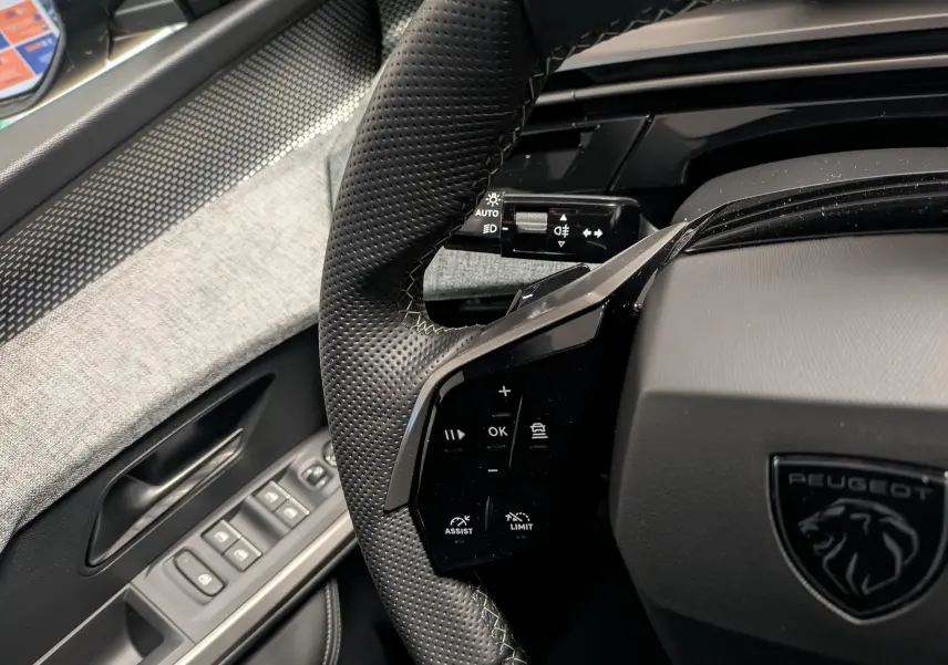 Gros plan sur le volant perforé noir avec surpiqûres vertes et commandes intégrées du Peugeot 3008 Hybrid 2025.