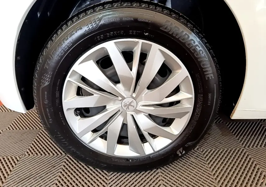 Gros plan sur la roue avant droite blanche d'une Peugeot 208 1.2 PT 75 S&S Premium avec jante argentée à design moderne.