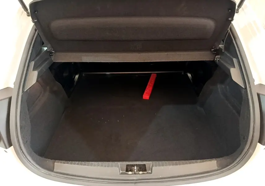 Coffre ouvert de la Peugeot 208 blanche vue de l'arrière, montrant un espace de chargement vide avec un triangle de signalisation rouge.