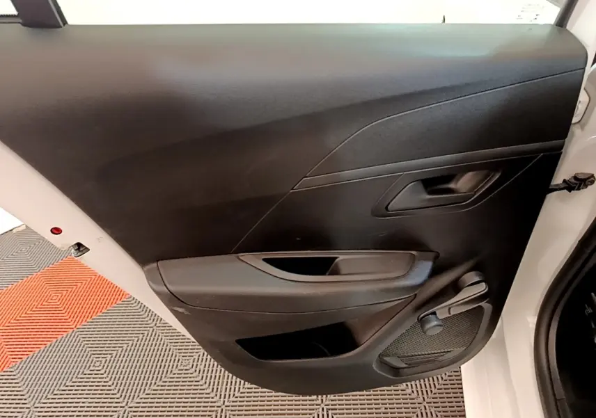 Vue rapprochée de la porte arrière droite noire d’une Peugeot 208 blanche, avec poignée et manivelle de vitre.