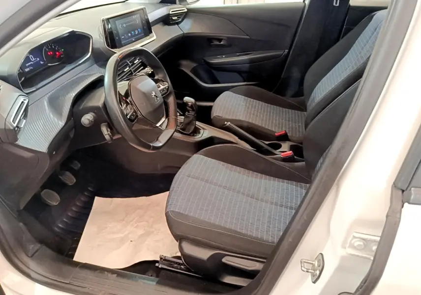 Intérieur de la Peugeot 208 blanc vue côté conducteur, montrant sièges tissu gris et tableau de bord numérique.