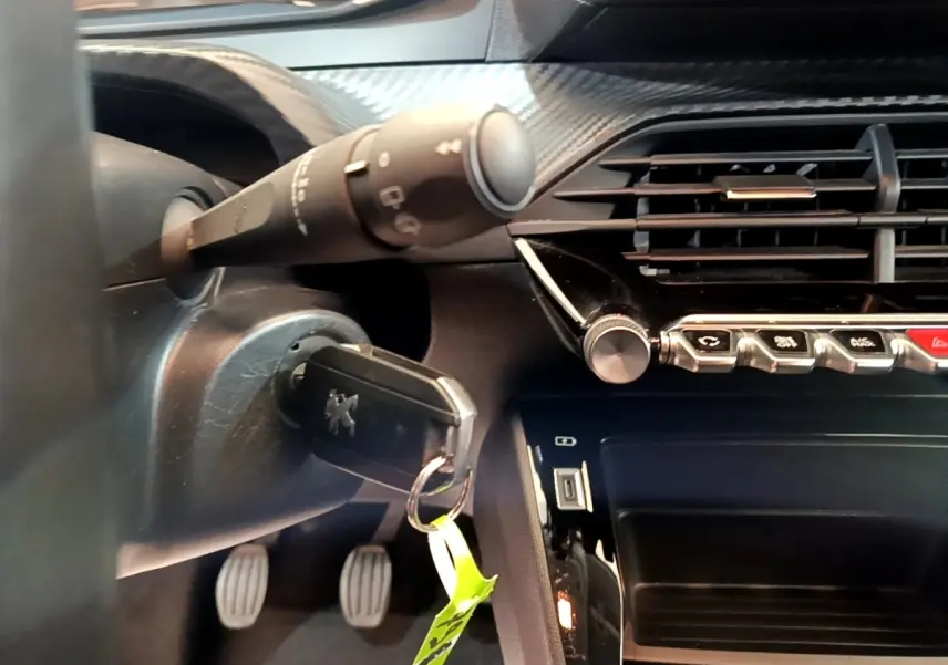 Vue rapprochée de l’intérieur côté conducteur de la Peugeot 208 blanche, avec clé insérée et commandes du tableau de bord visibles.
