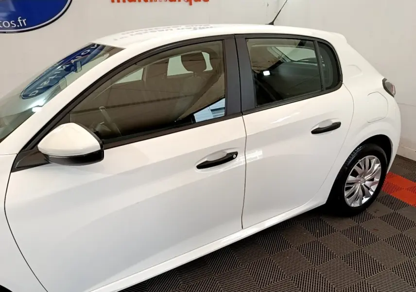 Profil côté gauche d'une Peugeot 208 blanche 2021, avec rétroviseur et poignées de porte visibles en intérieur showroom.
