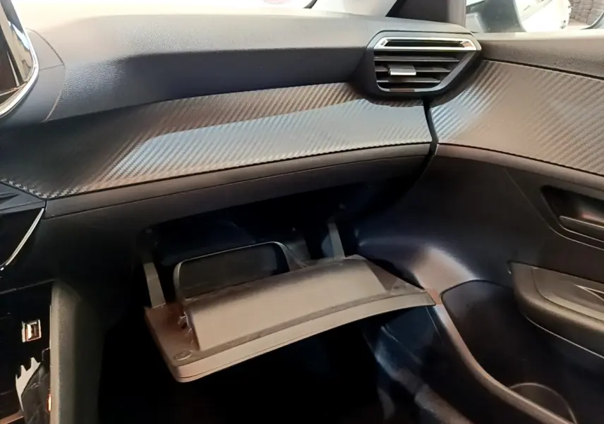 Intérieur de la Peugeot 208 2021, vue côté passager sur la boîte à gants ouverte et tableau de bord noir texturé.