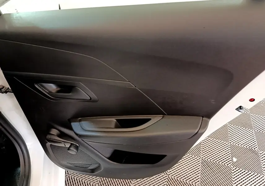 Vue rapprochée de la porte avant gauche blanche d’une Peugeot 208 2021 avec poignée et commande de vitre manuelle.