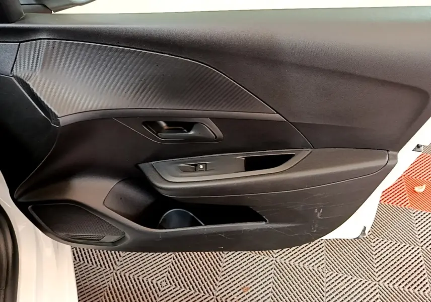 Vue intérieure de la porte avant gauche noire avec poignée et commande de vitre d'une Peugeot 208 blanche.