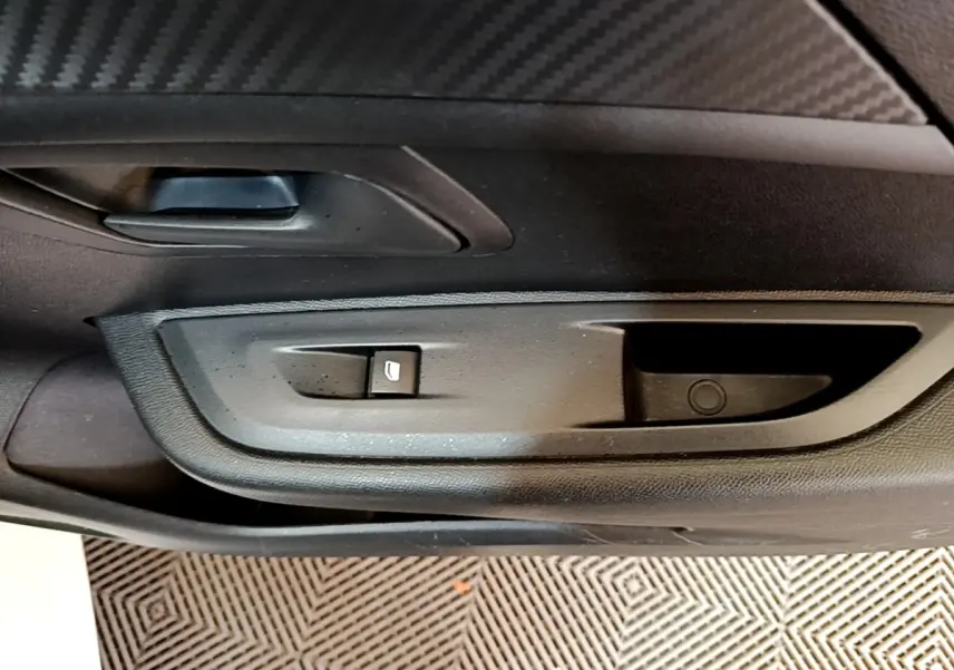Vue rapprochée de la porte intérieure côté gauche de la Peugeot 208 blanche, avec commande de lève-vitre et poignée noire.