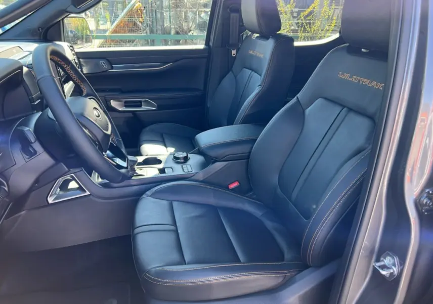Vue intérieure côté conducteur du Ford Ranger Wildtrak 2026, sièges cuir noirs avec surpiqûres orange et logo brodé.